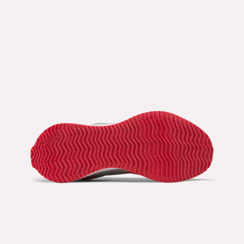The bottom view of the Reebok Pyro Storm Shoes - Big Kids displays a red sole with a wavy zigzag tread pattern, set against a plain white background. A small Reebok logo is visible on the left side near the toe, highlighting their design for kids’ running shoes.