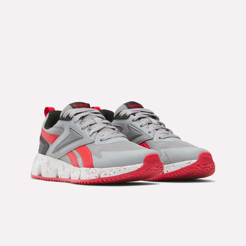 A pair of Reebok Pyro Storm Shoes - Big Kids is shown on a plain light background, featuring a gray design with red accents and white speckled soles. This lightweight pair is designed for running.