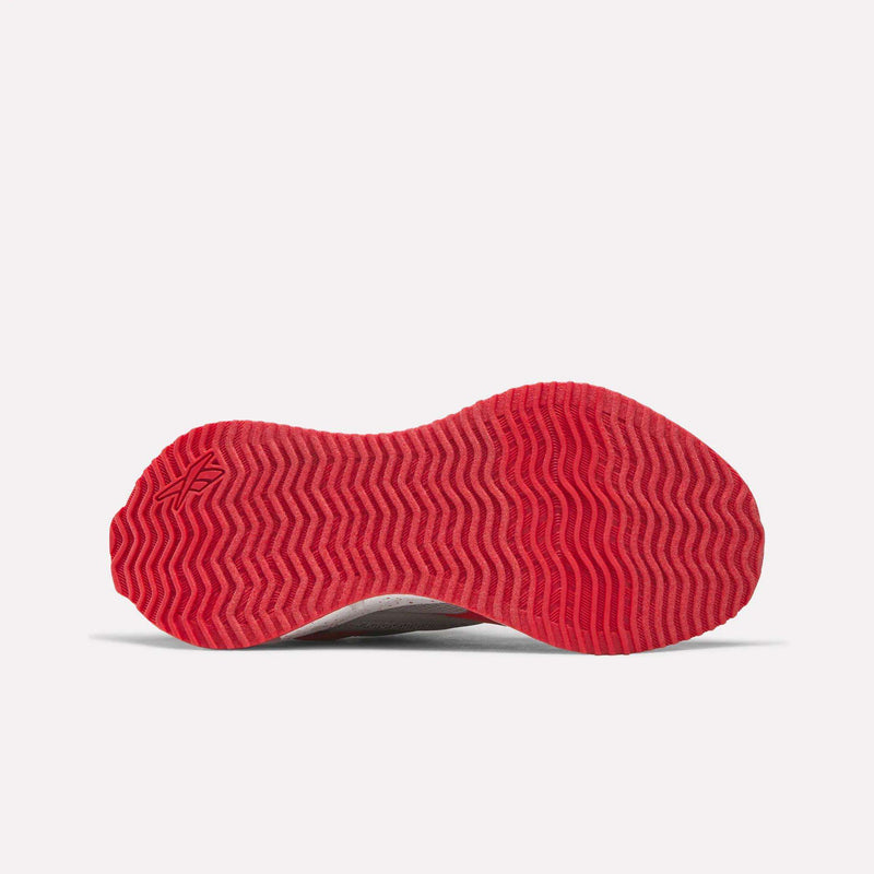 The image displays the bottom view of the Pyro Storm 1V Shoes - Little Kids by Reebok, showcasing a vivid red sole with a zigzag tread pattern against a plain white background. The robust rubber outsole emphasizes the quality craftsmanship of these shoes.