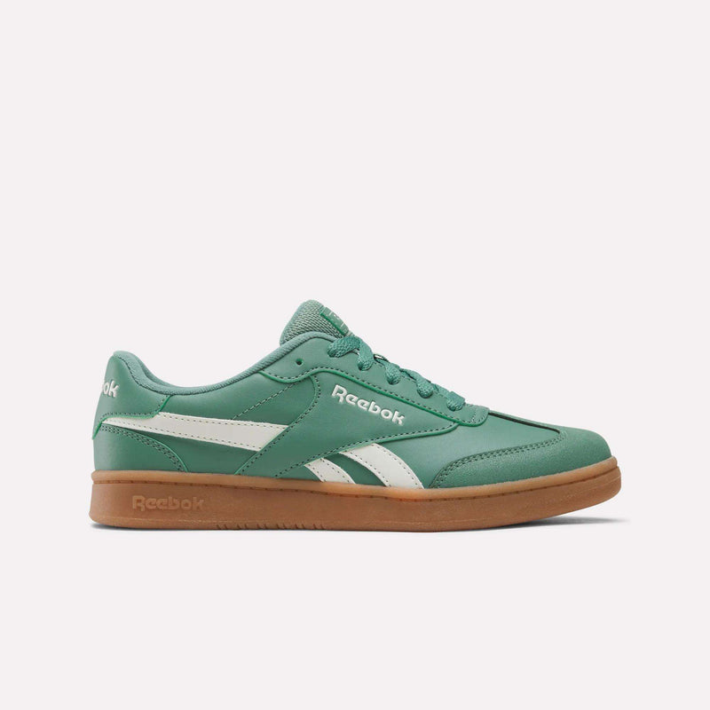 The Reebok Forte Pitch Shoes - Big Kids in Field Green feature a white logo, side stripes, and a gum-colored sole set against a white background. With classic styling inspired by court sneakers, these low-profile shoes have laces for a timeless look.