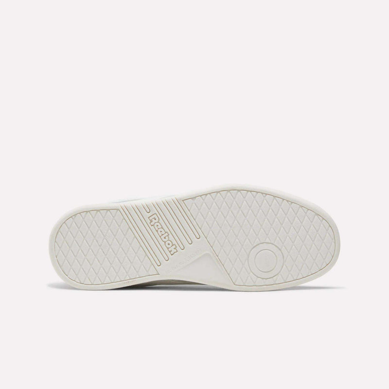 The image displays the white rubber sole of the Reebok Forte Pitch Shoes - Big Kids sneaker, shown from the bottom with a textured grip pattern, grooves, a circular mark, and the Reebok logo embossed in the center—emphasizing its court-inspired design.