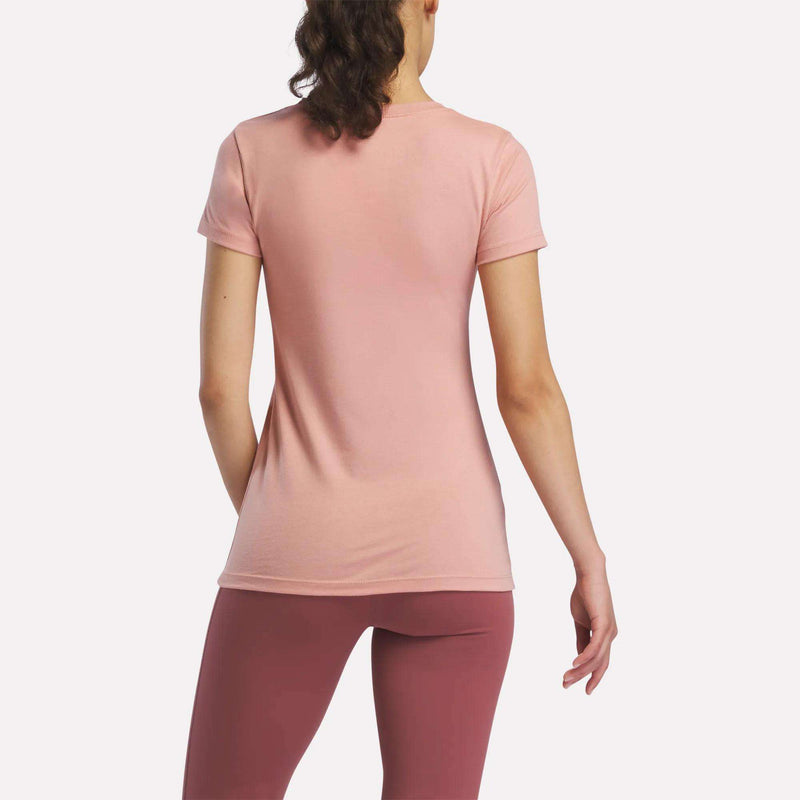 A woman with brown hair in a ponytail stands with her back to the camera, wearing a Reebok Women's T-Shirt and mauve leggings against a plain white background.