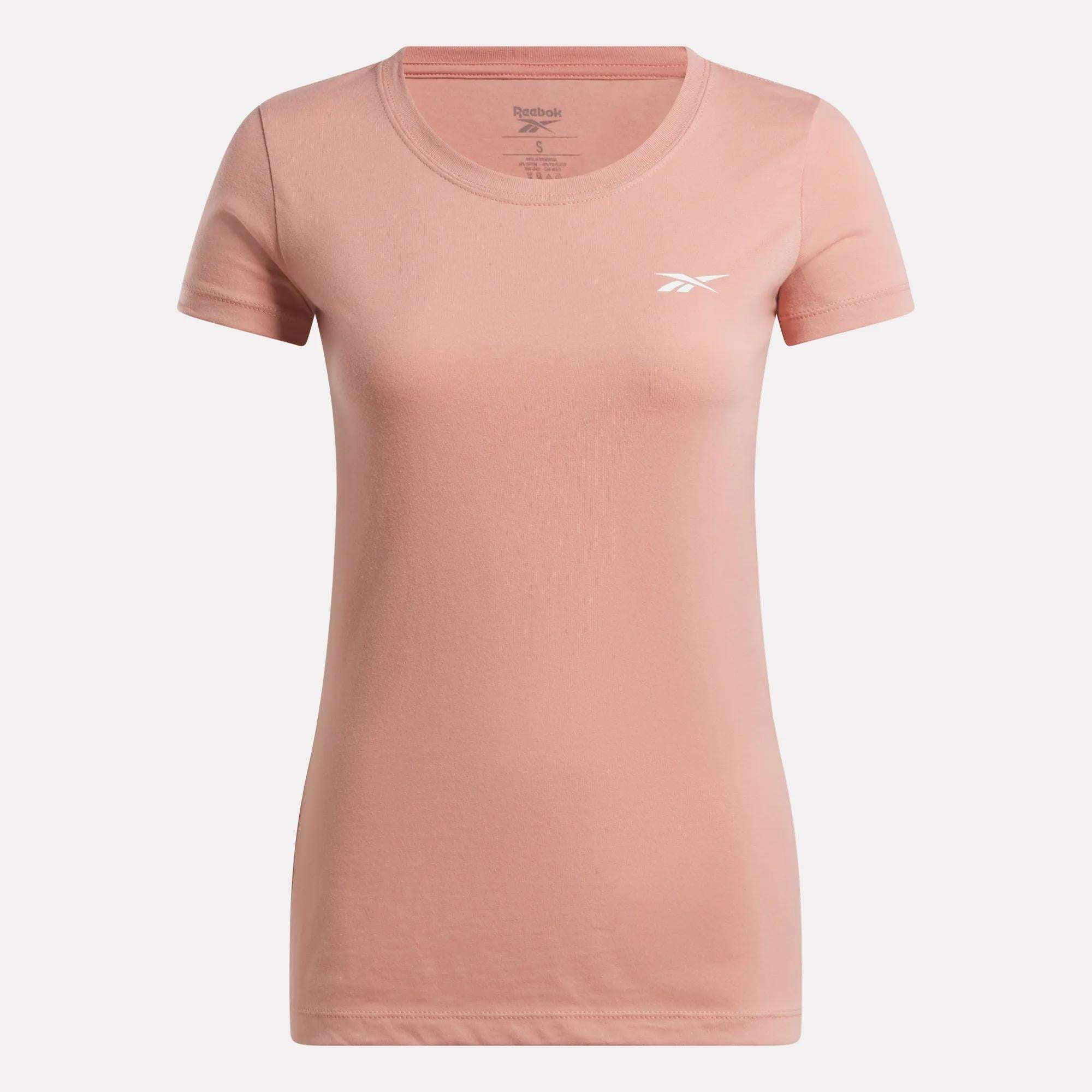 The Reebok Women's T-Shirt features a plain light pink cotton design with short sleeves, a round neckline, and a small white Reebok logo on the left chest, shown against a white background.