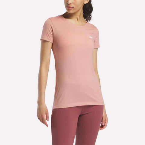 A woman in a fitted, short-sleeve light pink Reebok Women's T-Shirt stands against a plain white background.
