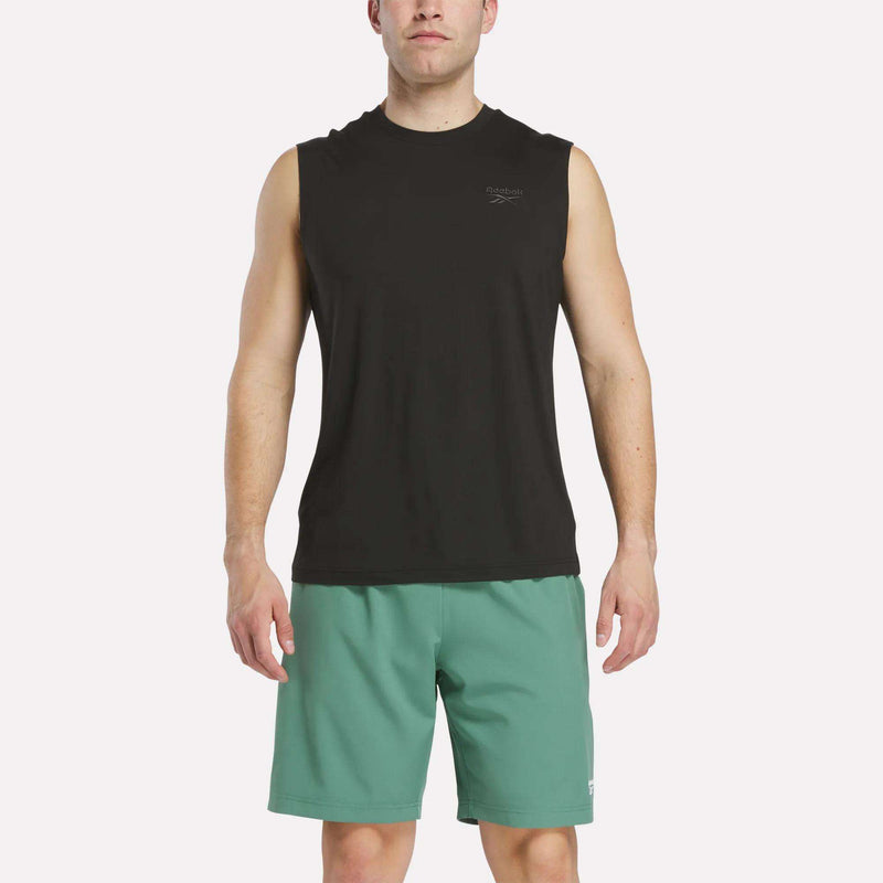 A man wearing a Reebok Men's Elite Sleeveless Top in Black Heather stands facing forward against a plain white background, paired with green shorts.