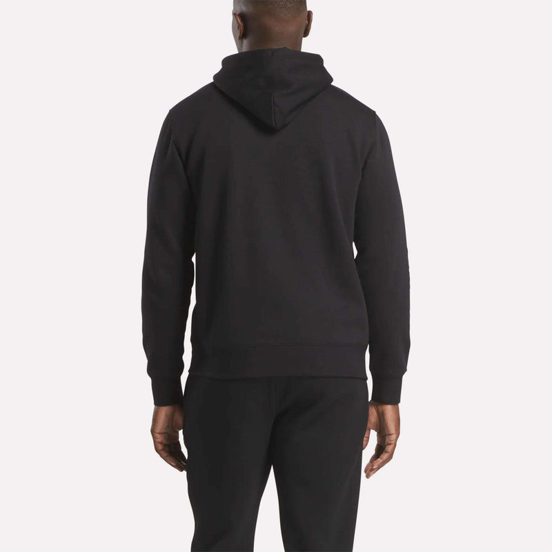 A person stands facing away from the camera, wearing the Reebok Men’s Finisher Hoodie and black pants against a plain light background.