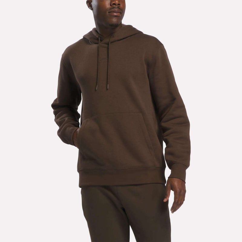 A man wearing the Reebok Men’s Finisher Hoodie, featuring a front pocket, along with matching brown pants stands against a plain white background.