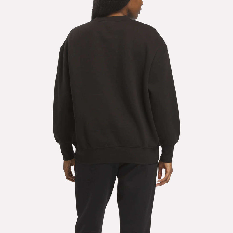 A person faces away from the camera, dressed in a relaxed silhouette that features the Reebok Women’s Oversized Crewneck Sweatshirt in black paired with black pants, set against a plain white background for an extra comfortable look.