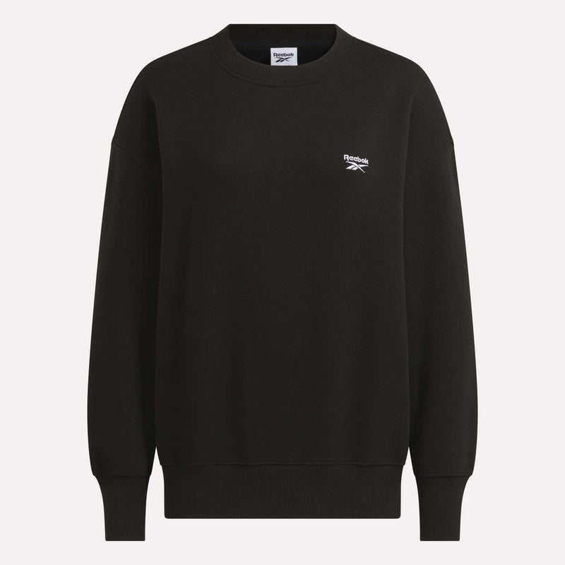 The Reebok Women’s Oversized Crewneck Sweatshirt is a black, long-sleeve pullover featuring a classic crewneck and ribbed cuffs and hem. This plain sweatshirt displays a small white Reebok logo on the left chest and is shown against a white background.