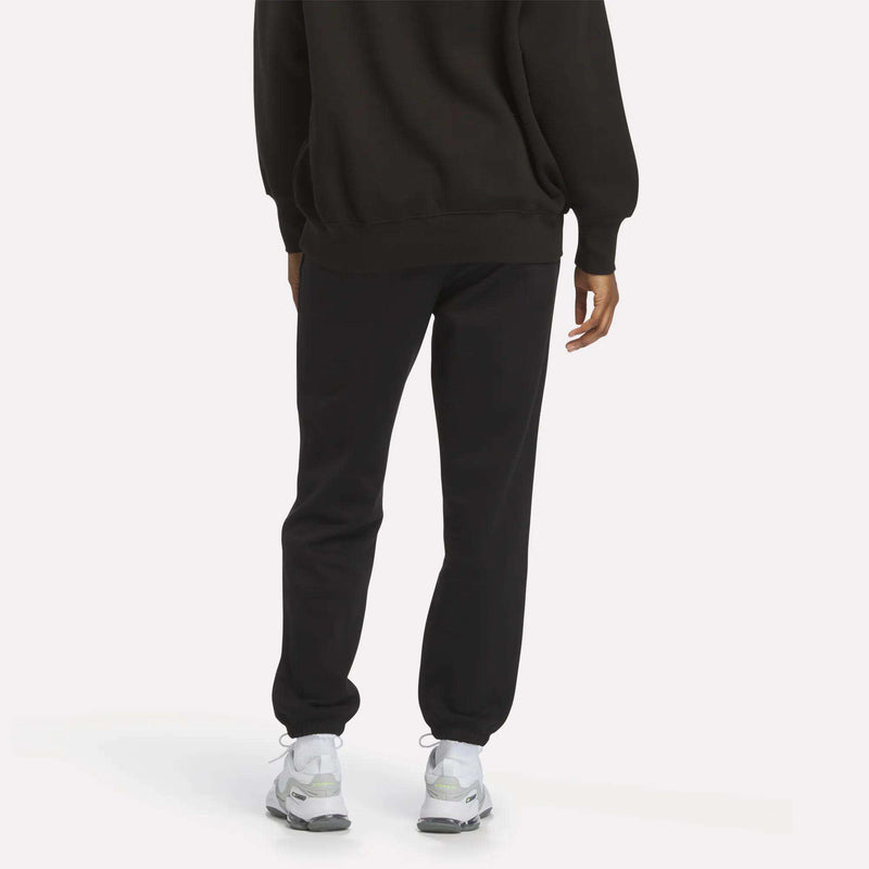 A person is seen from behind wearing Reebok Women’s Cinch Sweatpants with a modern design, paired with a black sweatshirt and white sneakers, set against a plain light background.
