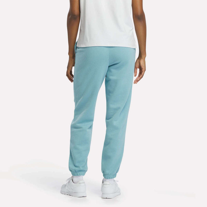 A person stands facing away, arms relaxed, wearing a white t-shirt, white sneakers, and light blue Reebok Women’s Cinched Sweatpants against a plain light background.
