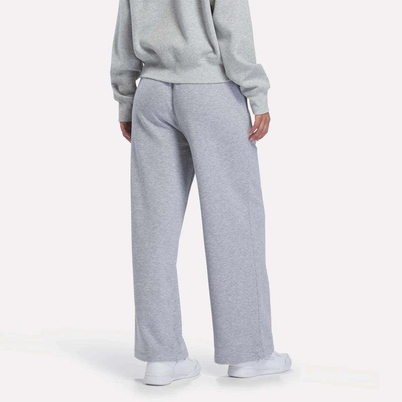 A person is shown from the back wearing Reebok Women’s Wide-Leg Sweatpants in gray, paired with a matching gray sweatshirt and white sneakers, standing against a plain white background.