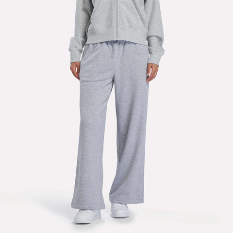 A person dressed in Reebok Women’s Wide-Leg Sweatpants in Grey Heather, styled with a matching gray zip-up hoodie and white sneakers, stands against a plain white background with their face not visible.