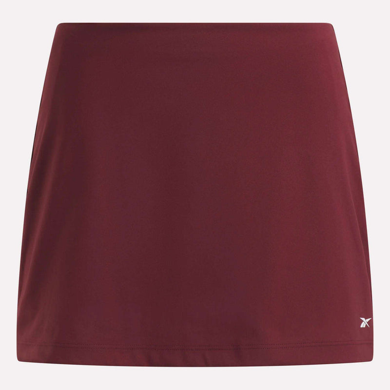This Reebok Women’s Tennis Skort is a plain maroon athletic skirt with a subtle white logo near the bottom right hem, featuring built-in shorts for extra comfort and coverage, shown against a white background.