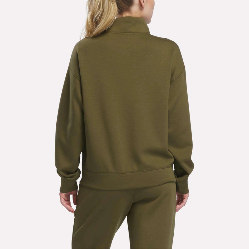 A person with long blonde hair in a ponytail is shown from the back against a plain white background, wearing a Reebok Women’s Crop Half-Zip Sweatshirt in olive green with matching pants.