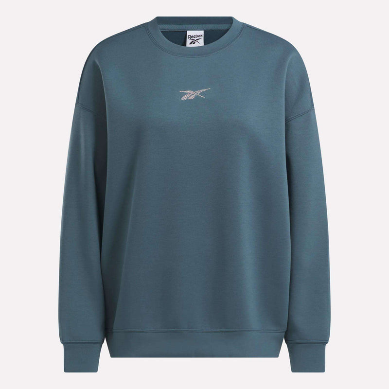 The Women’s Relaxed Crewneck Sweatshirt by Reebok is displayed front-facing against a plain backdrop, in a blue-green color. It showcases a small embroidered Reebok logo at the center chest and features a roomy, relaxed silhouette for comfortable everyday wear.