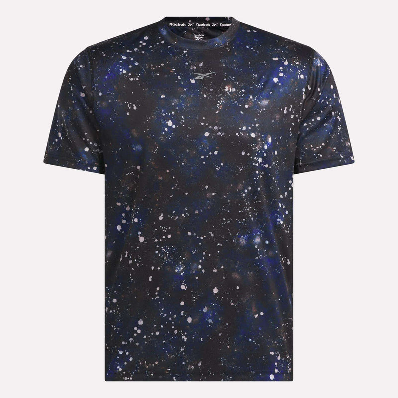 Introducing the Reebok Men’s Running Short Sleeve Tee, featuring a black base with an abstract splatter pattern in blue, white, and gray that evokes a galaxy or space theme. This lightweight t-shirt combines eye-catching style with performance, making it perfect for workouts or casual outings.