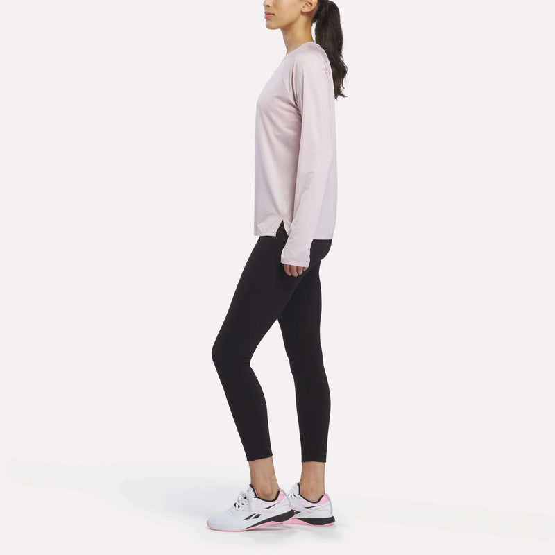 A person wearing the Reebok Women’s Long Sleeve Running Top, black leggings, and white sneakers stands in profile against a white background.