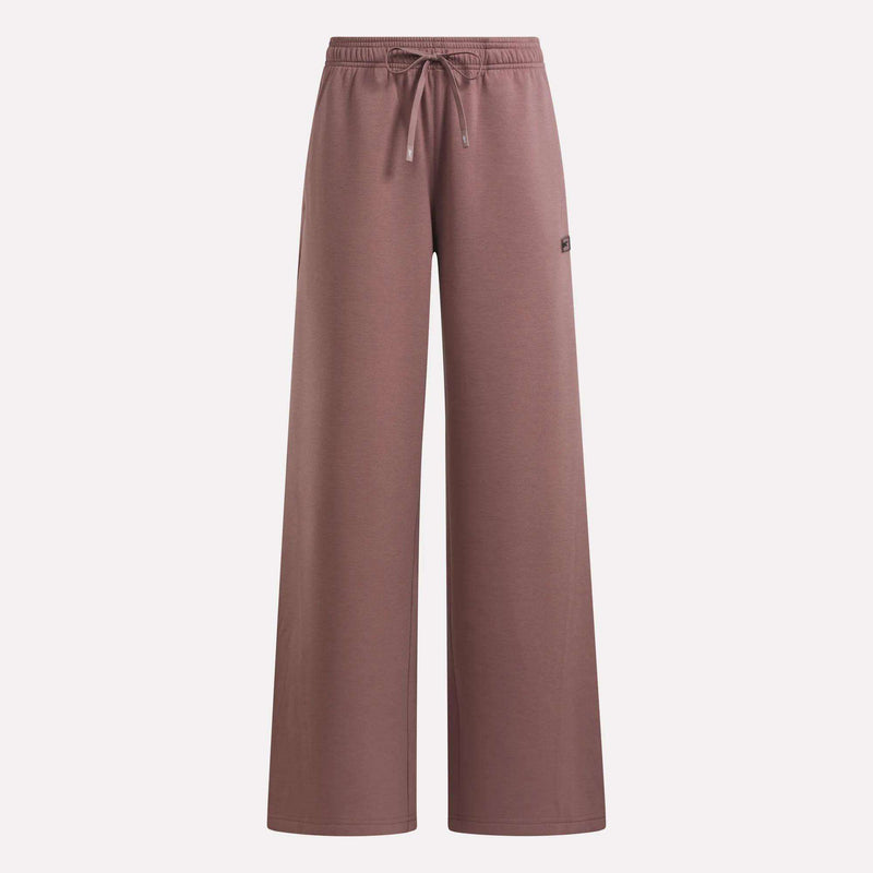 The Reebok Women’s Mid-Rise Wide-Leg Pants in mauve offer everyday comfort with their relaxed silhouette, comfortable pull-on waistband, and adjustable drawstring. A small Reebok logo patch accents the upper left side. Shown against a plain white background, these pants are ideal for women seeking both style and ease.