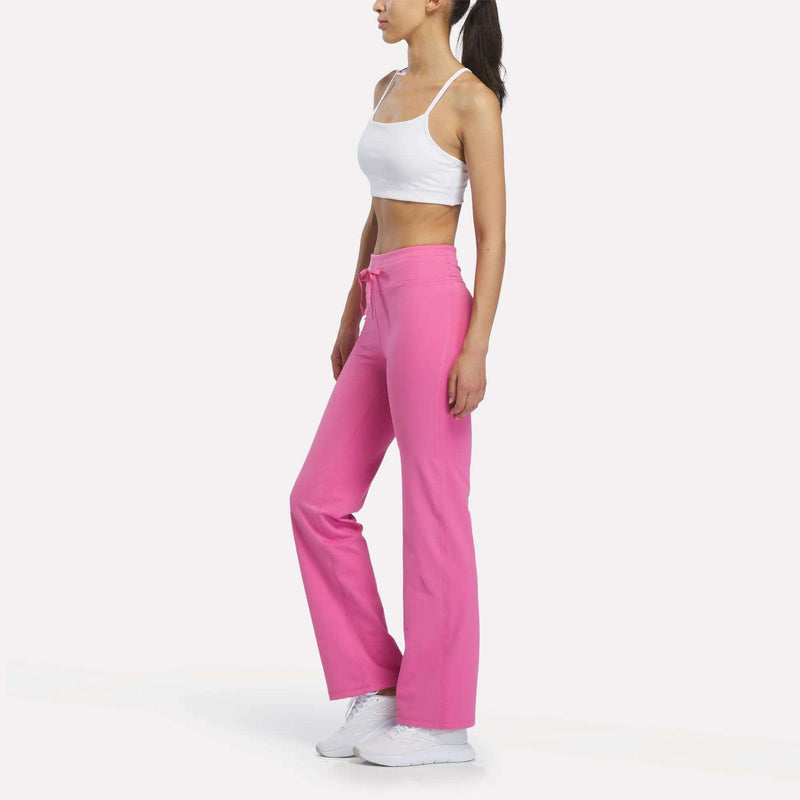 A woman wearing a white sports bra and bright pink Reebok Women’s Highstreet High-Rise Pants with white sneakers.