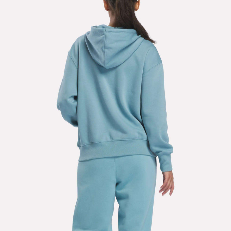 A person with a ponytail is shown from the back, wearing a light blue Reebok Women’s Oversized Full-Zip Hoodie and matching sweatpants against a plain white background.