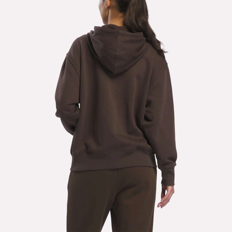 A person stands facing away from the camera, wearing a Reebok Women’s Oversized Full-Zip Hoodie against a plain white background.