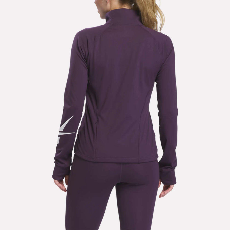 A woman with a blonde ponytail is shown from the back wearing a fitted, long-sleeve, purple Reebok Women’s Motion Core Full-Zip jacket and matching leggings. The jacket features a white graphic visible on one sleeve.