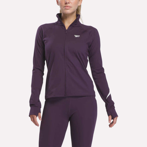 A woman wears a fitted, long-sleeve Reebok Women’s Motion Core Full-Zip jacket and matching leggings in Phantom Purple. The jacket features RBK-DRY technology for comfort and displays a small white Reebok logo on the chest. The background is plain white.