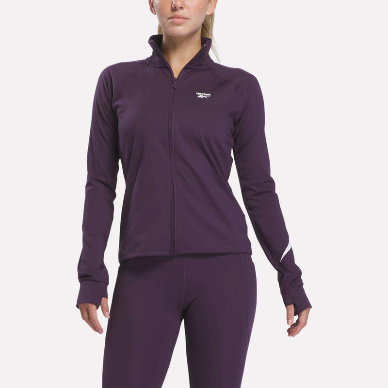 A woman wears a fitted, long-sleeve Reebok Women’s Motion Core Full-Zip jacket and matching leggings in Phantom Purple. The jacket features RBK-DRY technology for comfort and displays a small white Reebok logo on the chest. The background is plain white.