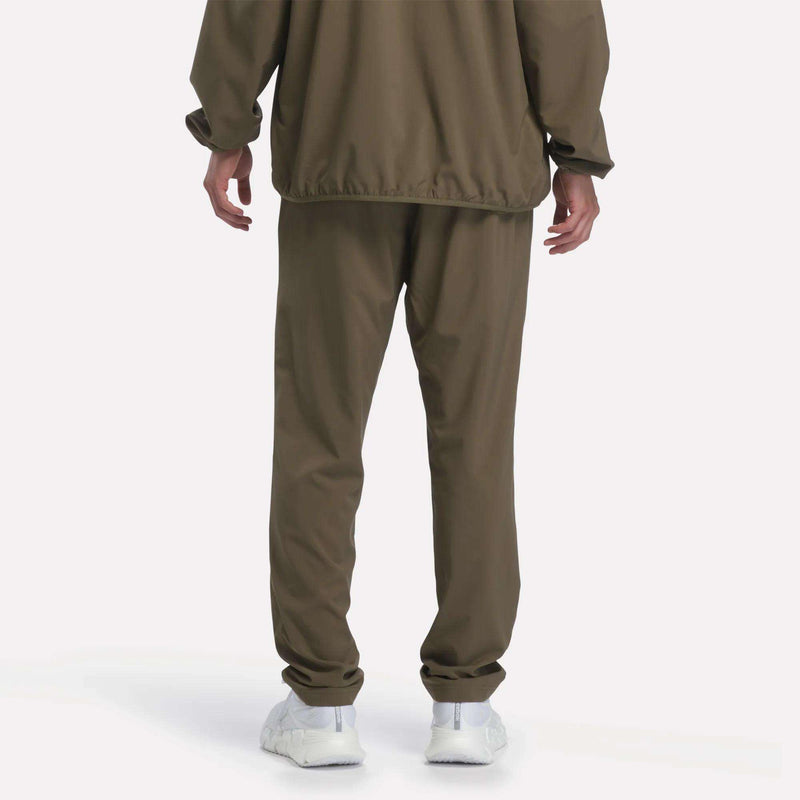 Back view of a person wearing olive green Men’s Woven Training Pants and a matching Reebok windbreaker with white sneakers.