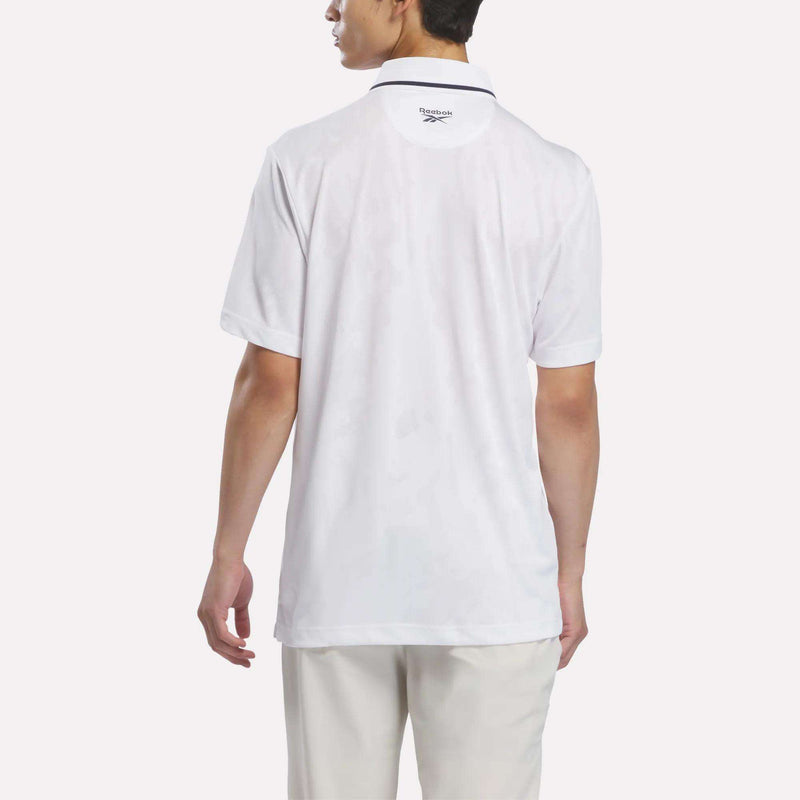 A person is shown from the back, facing away from the camera against a plain background, wearing a white short-sleeve Men’s Tournament Polo Shirt by Reebok and white pants.