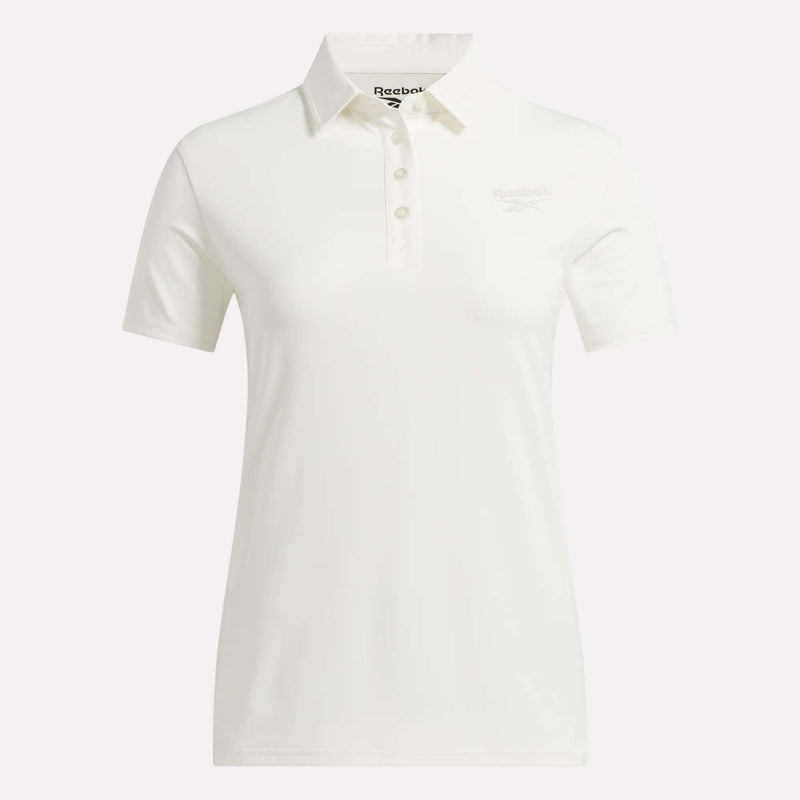 The Reebok Women's Solid Core Polo Shirt is a white, short-sleeve golf top featuring a classic collar and button placket. Made from performance jersey for comfort and breathability, it displays a subtle Reebok logo on the left chest. The shirt is shown against a plain white background.