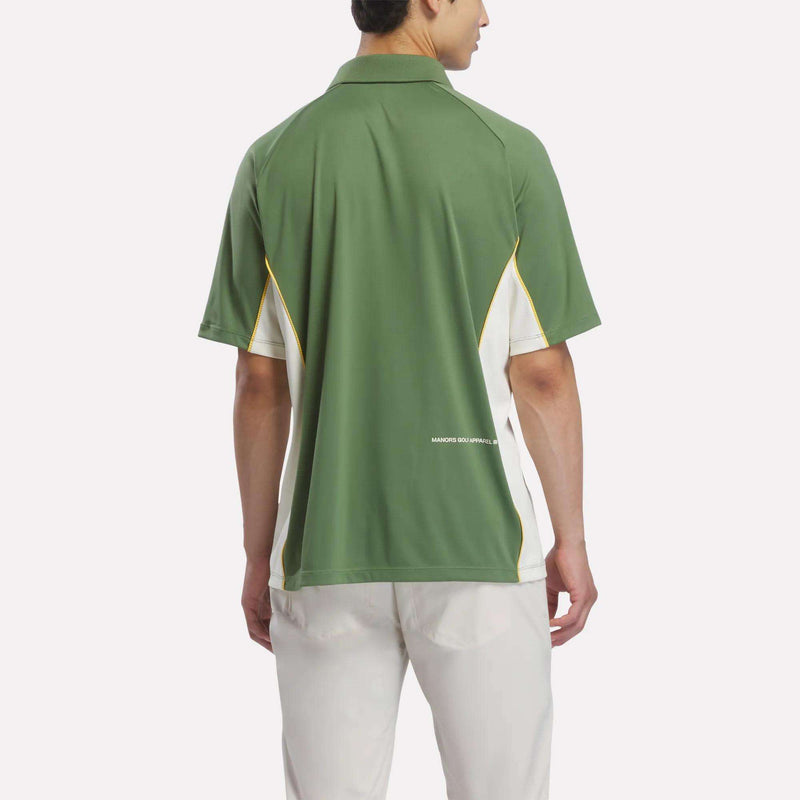 A person wearing the Reebok x Manors Men’s Polo in green and white with white pants stands facing away, highlighting the back of the polo shirt by Reebok.