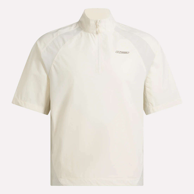 Introducing the Reebok x Manors Men’s Tour Shirt: a short-sleeve, off-white men’s golf pullover featuring a quarter-zip collar and a small oval logo on the left chest. Designed with relaxed fit and subtle panel detailing at the shoulders and sides, this shirt is part of the exclusive Reebok x Manors collection.