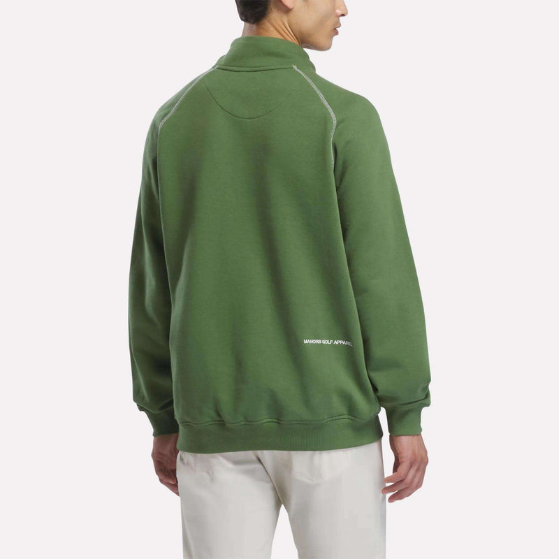 A person wearing a green Reebok x Manors Men’s Quarter-Zip Pullover and white pants stands facing away, displaying the back of the sweatshirt with “MAJOR GOLF APPAREL” text near the hem, from the Reebok collection.