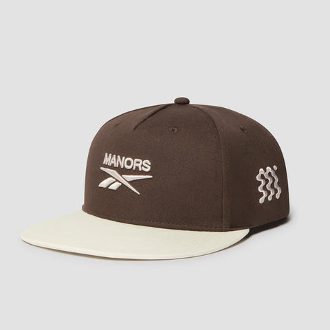 Introducing the Reebok x Manors Men’s Retro Crown Cap: this brown golf cap features a cream-colored brim and an adjustable snapback closure. Embroidered with MANORS and a logo on the front, plus a distinctive white wavy design on the side, its retro crown delivers classic style to this standout piece from Reebok.