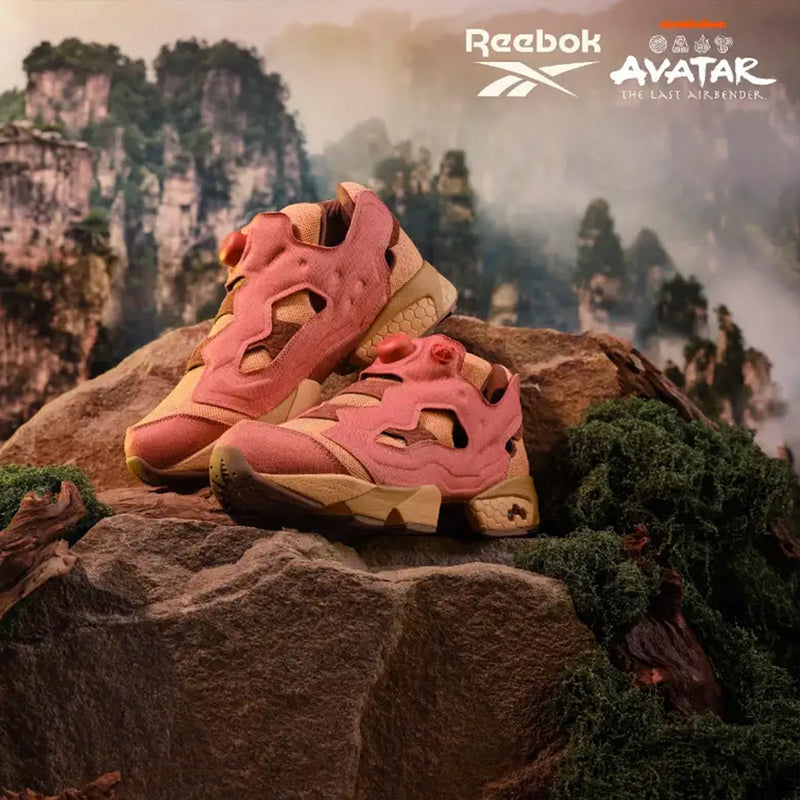 Two pink and tan Reebok x Avatar Instapump Fury 94 Shoes with textured detailing displayed on a mossy rock against a mountainous landscape backdrop.
