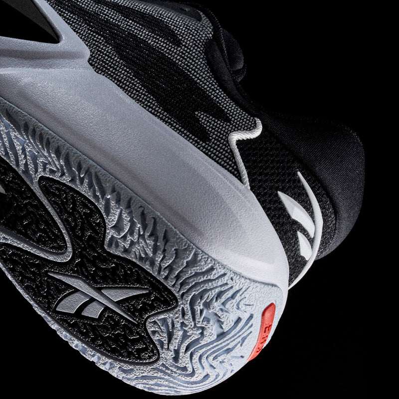 Close-up of the heel and sole of a black and white Reebok Engine A 26 basketball shoe, featuring a textured tread pattern and a logo on the outer heel.