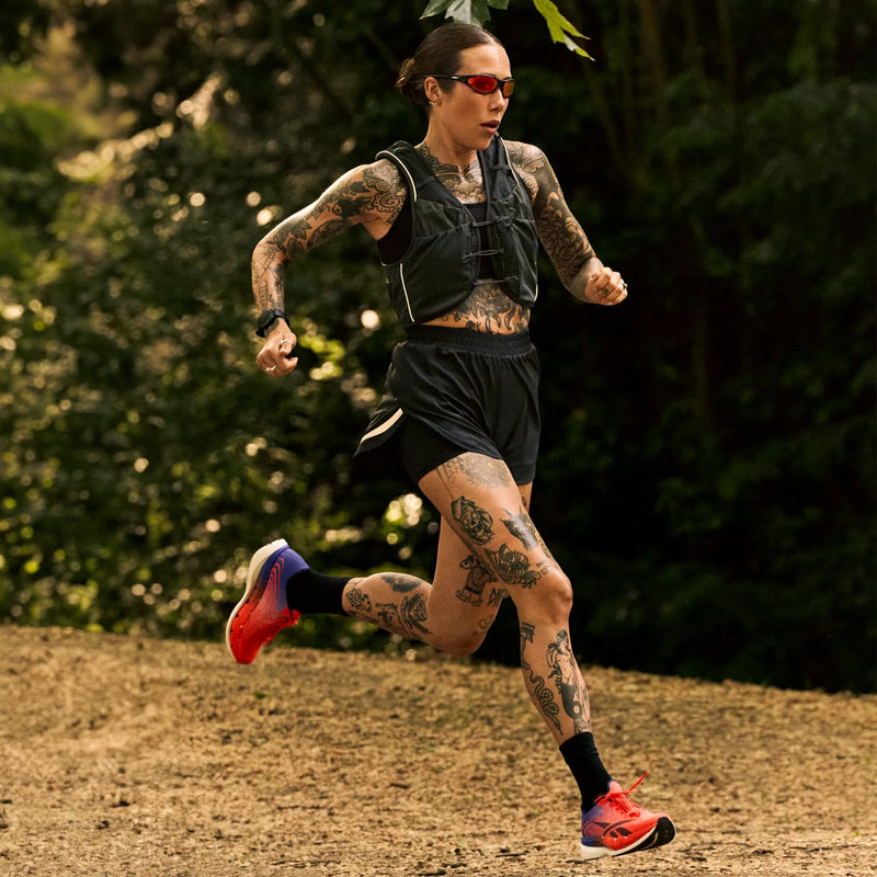 A tattooed runner wearing a black vest and shorts runs along a dirt path in Reebok SpeedShifter running shoes.