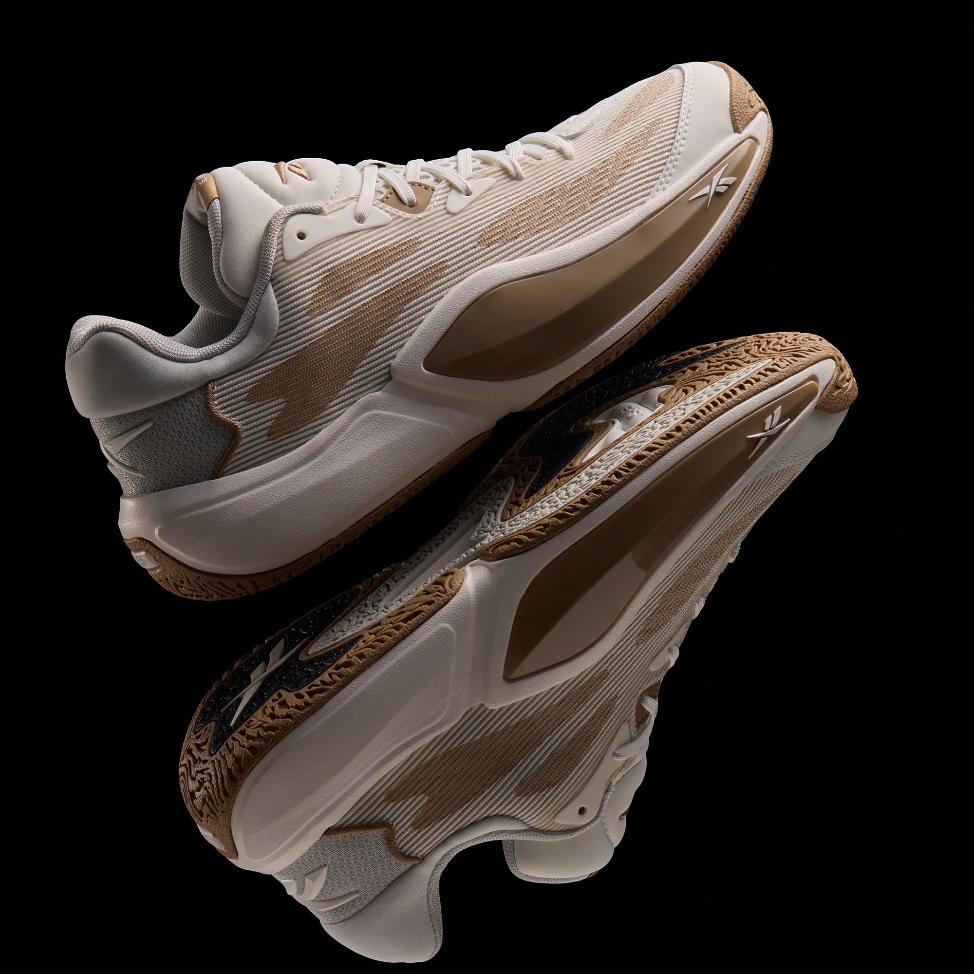 The Reebok Engine A 26 Basketball Shoes feature beige and tan uppers, textured soles, white laces, and mesh detailing for enhanced stability, elegantly reflected on a glossy black surface.