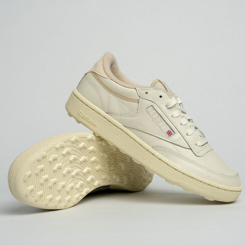 A pair of off-white Reebok Women's Club C Golf Shoes, crafted with water-resistant leather—one upright, the other tilted to show its textured sole—are displayed against a simple light grey background.