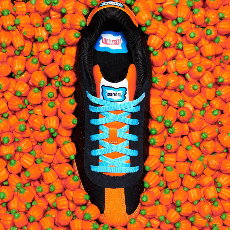 Black and orange Reebok x Icecream Board Flip shoes with bright blue laces, centered in a bed of small orange pumpkin candies.