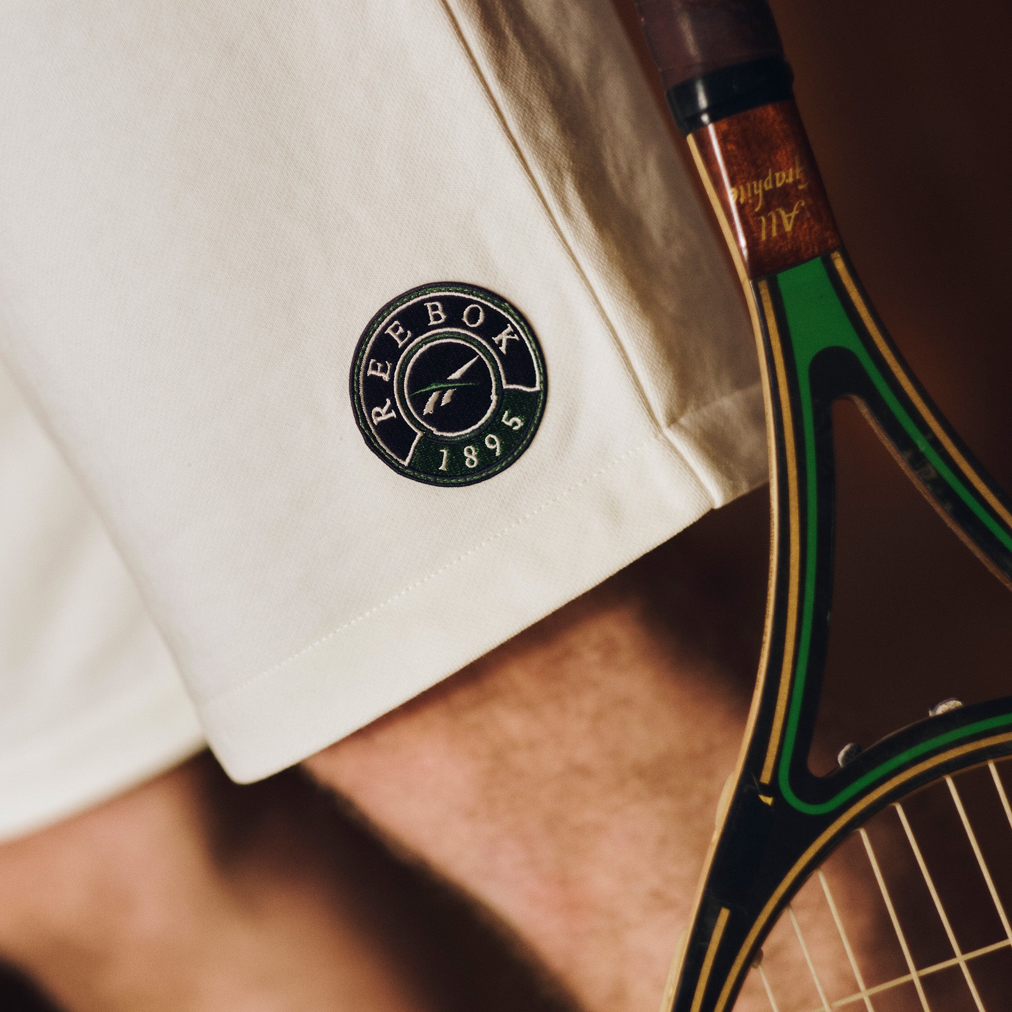 Person wearing a white shirt with a Reebok logo holding a tennis racket.
