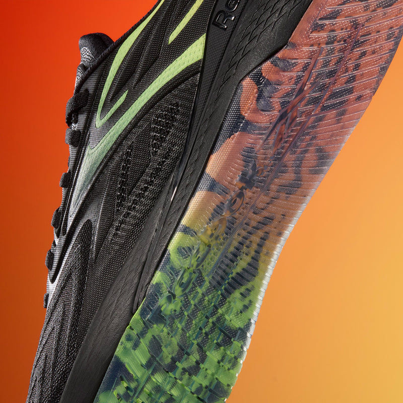 Close-up of Reebok Nano X5 Edge Training Shoes in black with green accents, showing a textured upper and a transparent multicolored sole—where performance meets style—backdropped by a vibrant red-to-orange gradient.