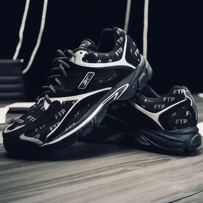Black and white sneakers with visible branding on a wooden floor.