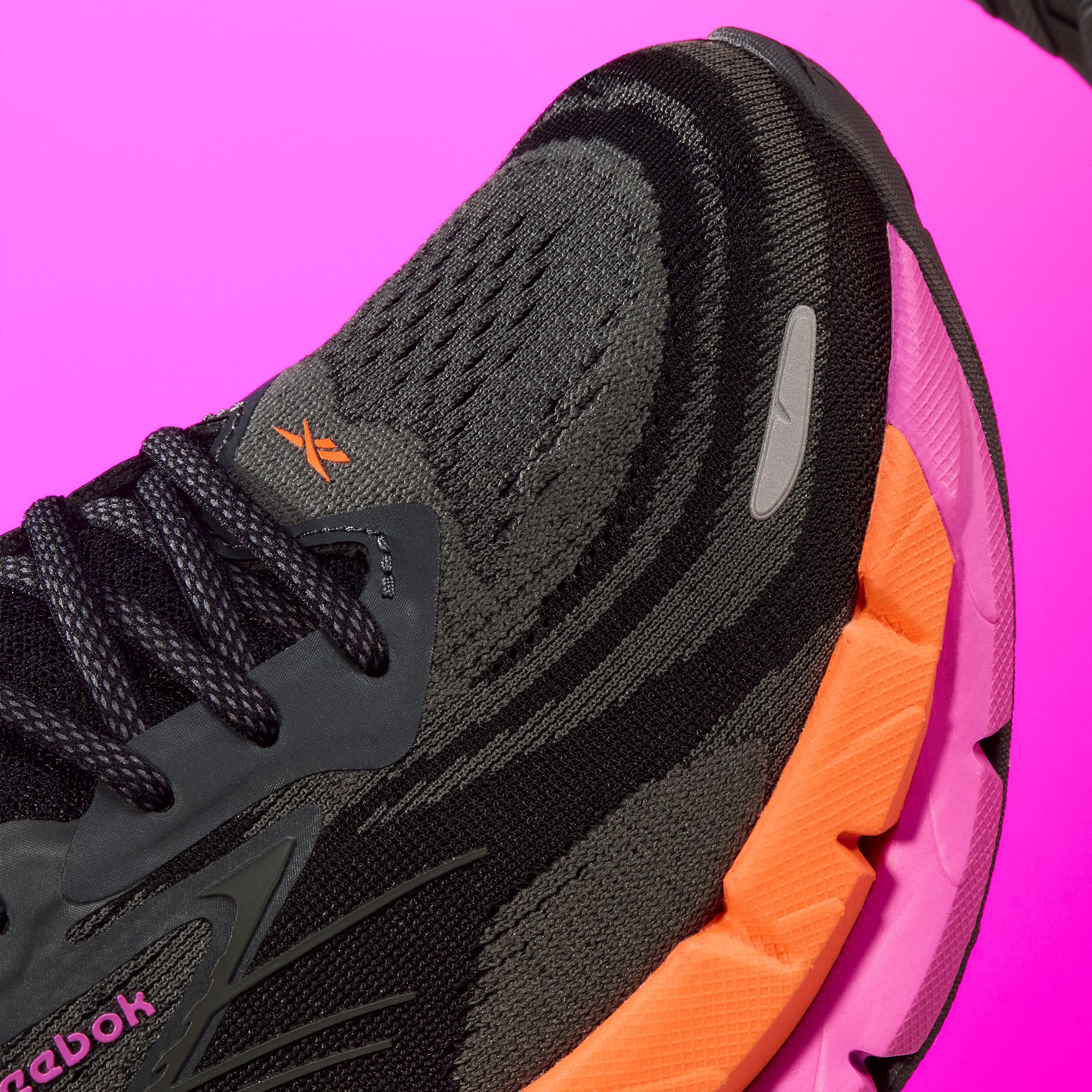 Black and orange Reebok sneaker on a pink background