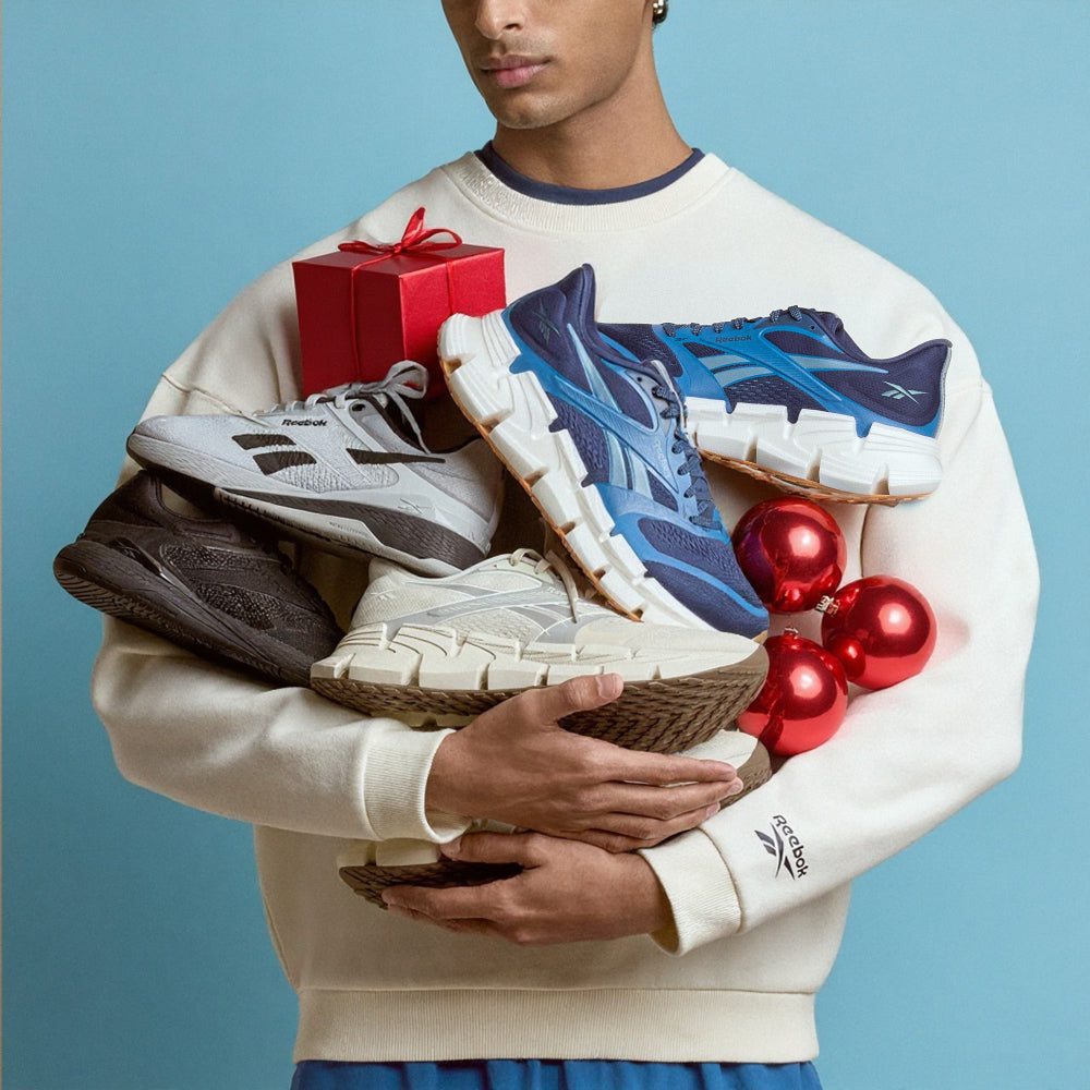 Person holding various sneakers and a red gift box against a blue background