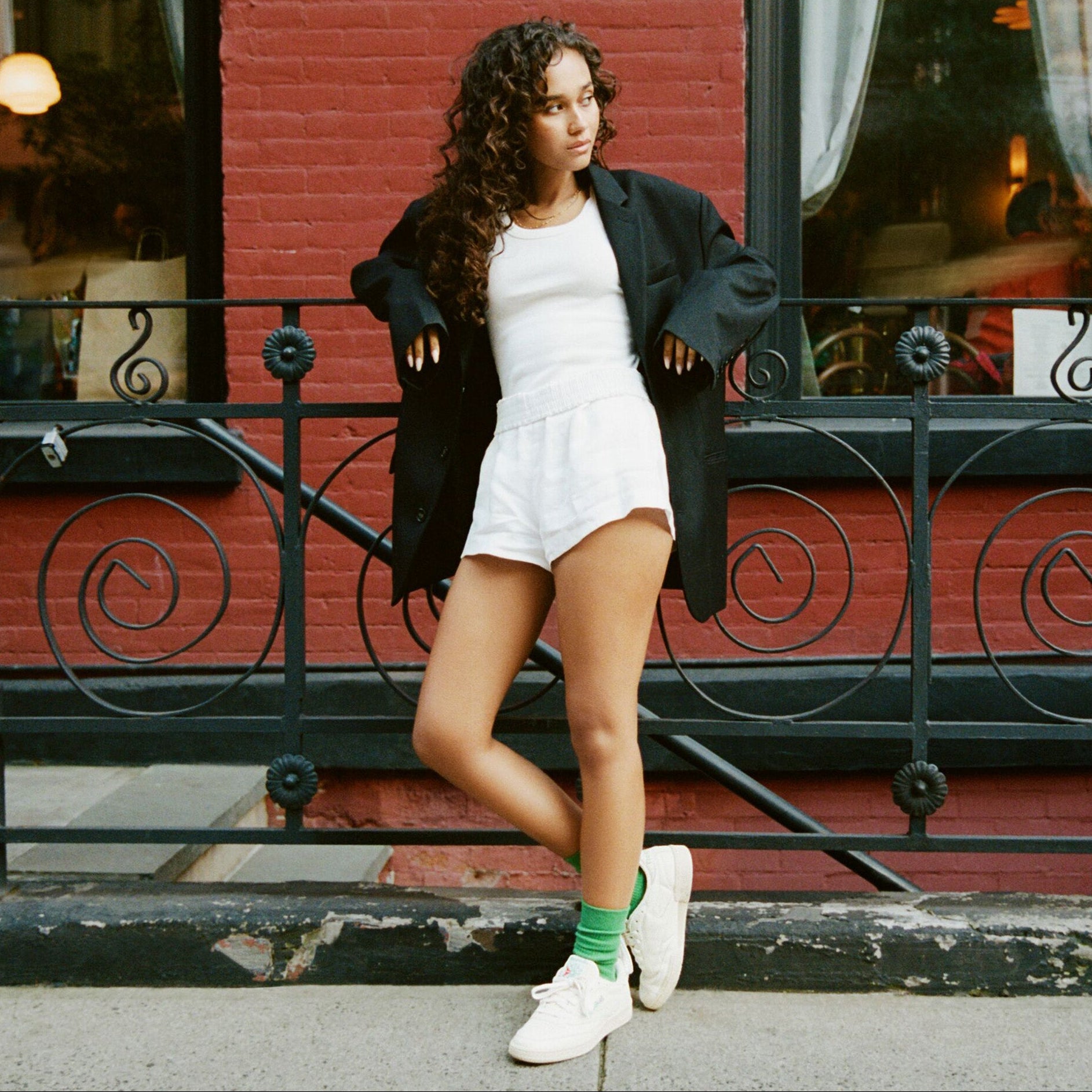Woman in a white outfit standing on a street with a red brick building in the background