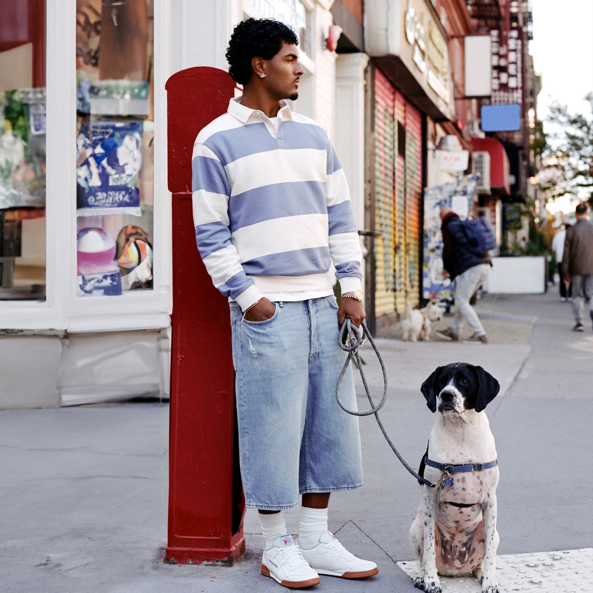 A man wearing Reebok shoes on a street with a dog on a leash.