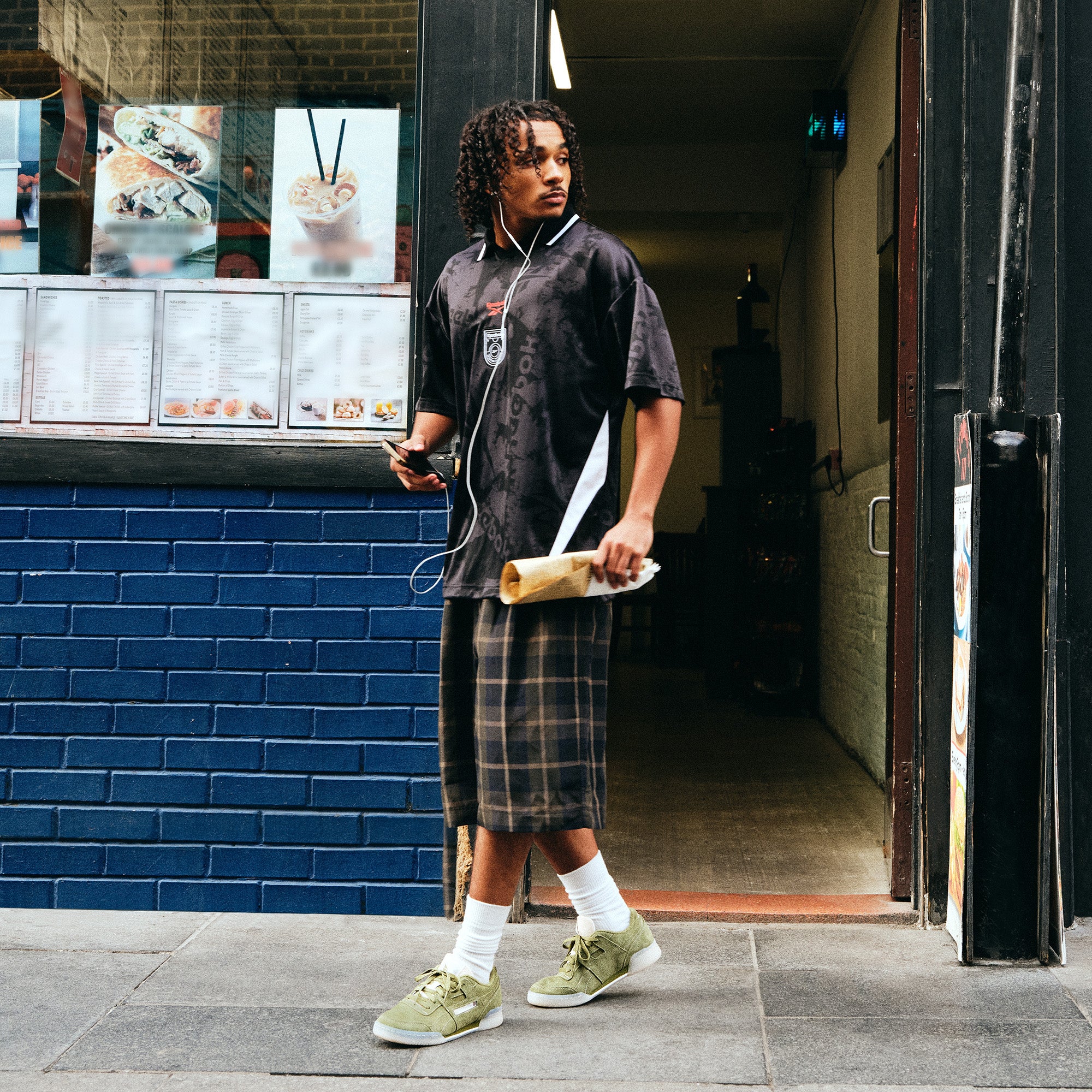 A man wearing Reebok shoes walking down a city sidewalk.